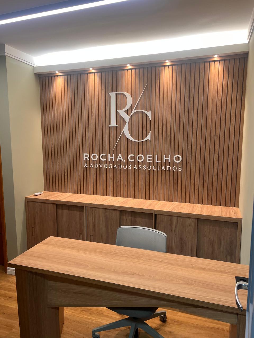 Imagem da recepção do escritório, com uma mesa, uma cadeira e uma parede estilizada com o logo da empresa.